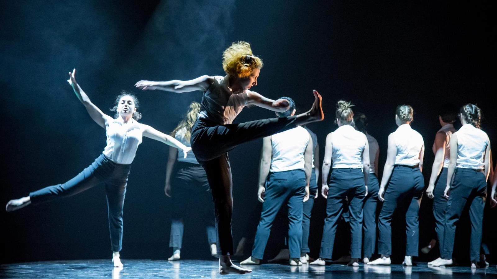 Two students dance downstage while several others stand upstage in a line