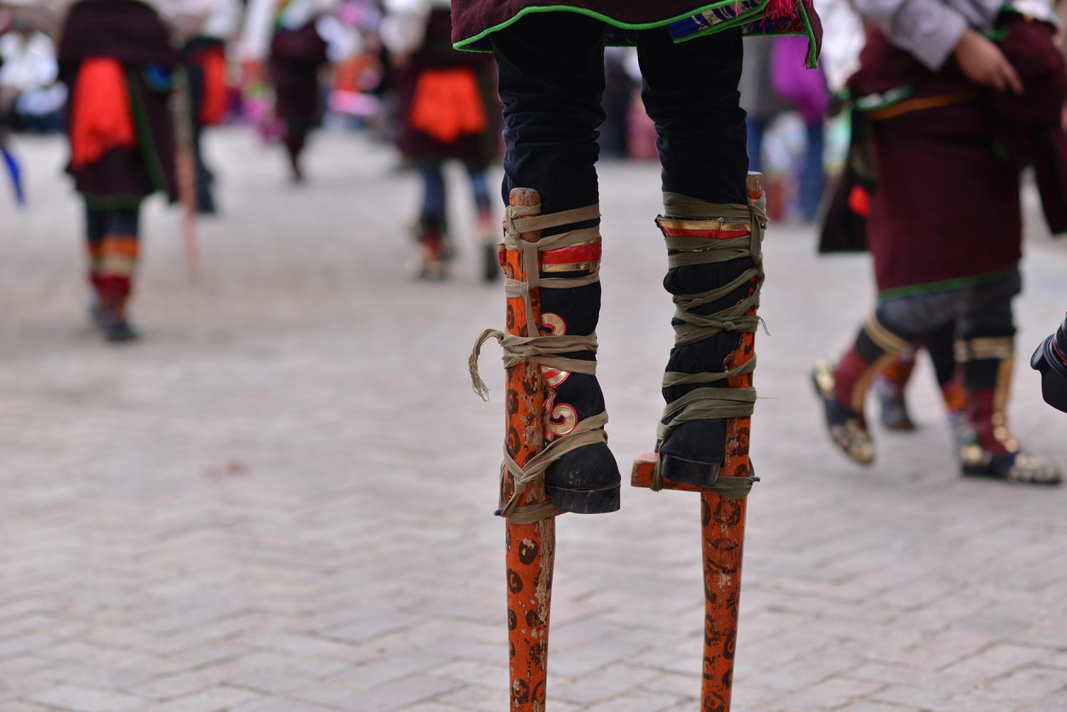 A young man wears stilts as he dances around the courtyard on stilts or “wooden feet” called Kang hung (Rkang shing, རྐང་ཤིང་).