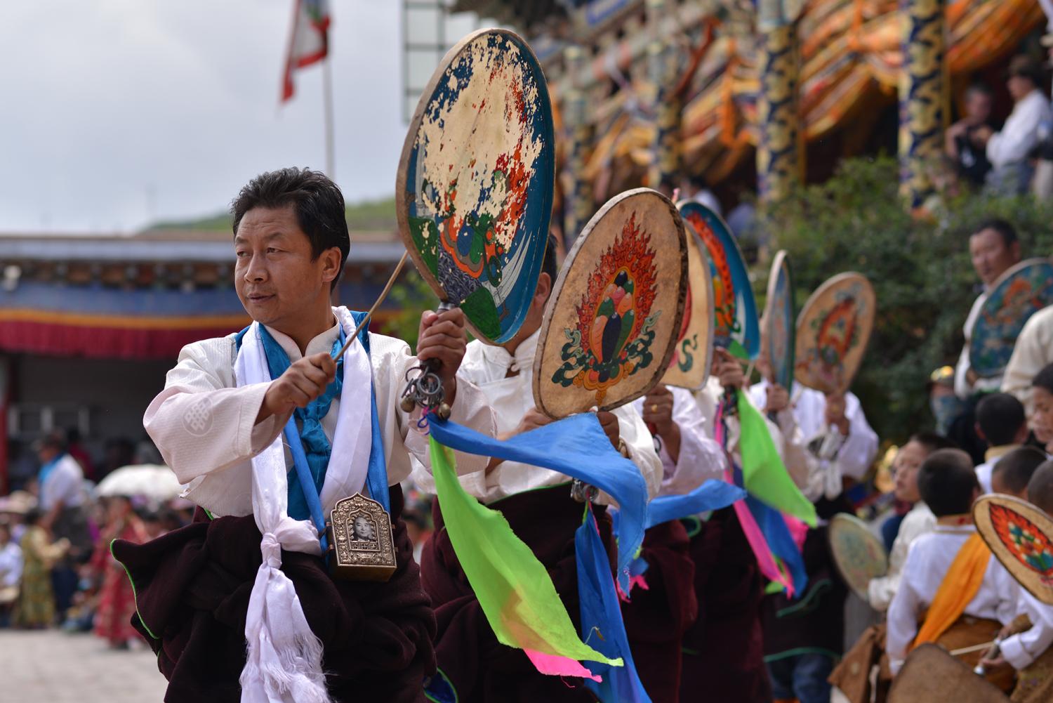 Men perform La tsey (Lha rtsed ལྷ་རྩེད), or “God Play,” by beating small drums while moving in a rhythmic regimented pattern.