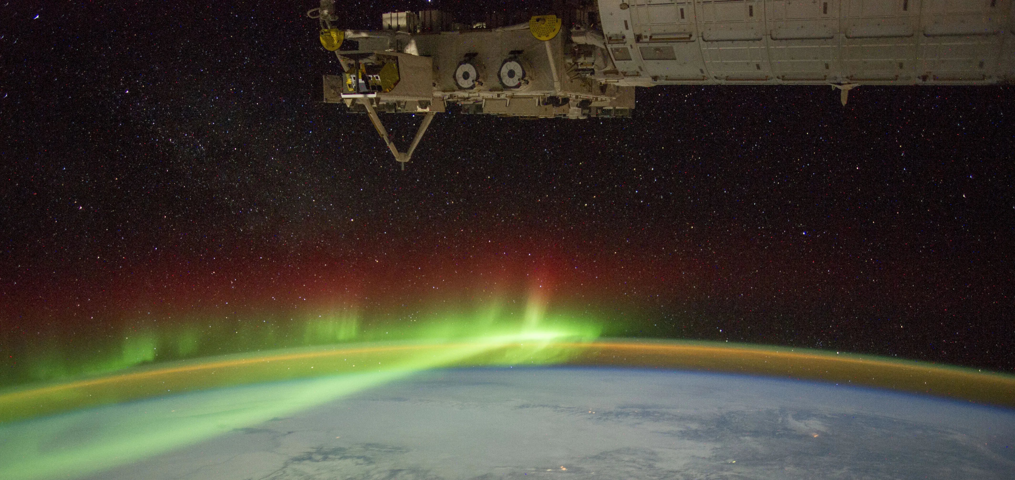 Spacecraft orbits above Earth, with an aurora shining in its atmosphere