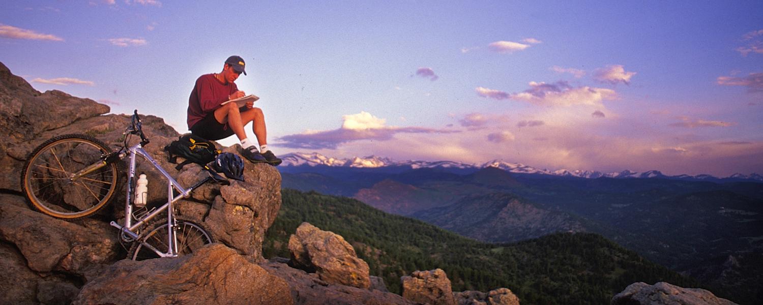 Bicyclist looking at a sunset atop a rock outcropping on a mountain