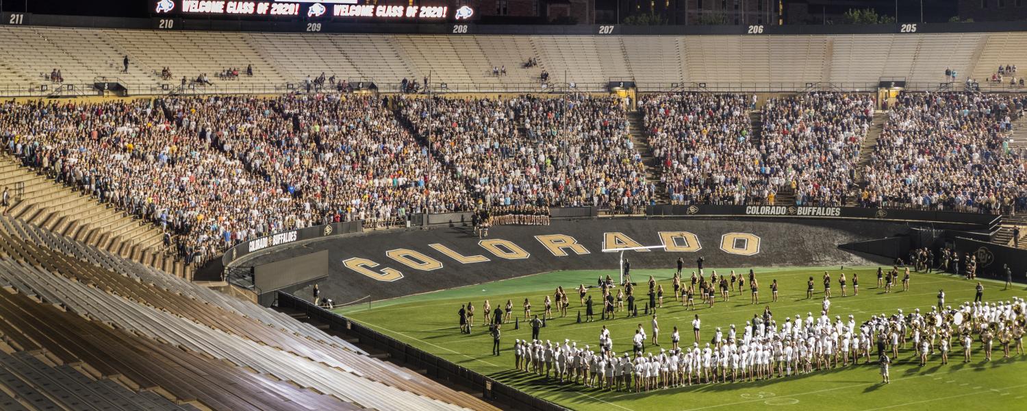 The Class of 2020 sit in the stands in Folsom Stadium, stretching across several sections, while the band and spirit squad are on the field