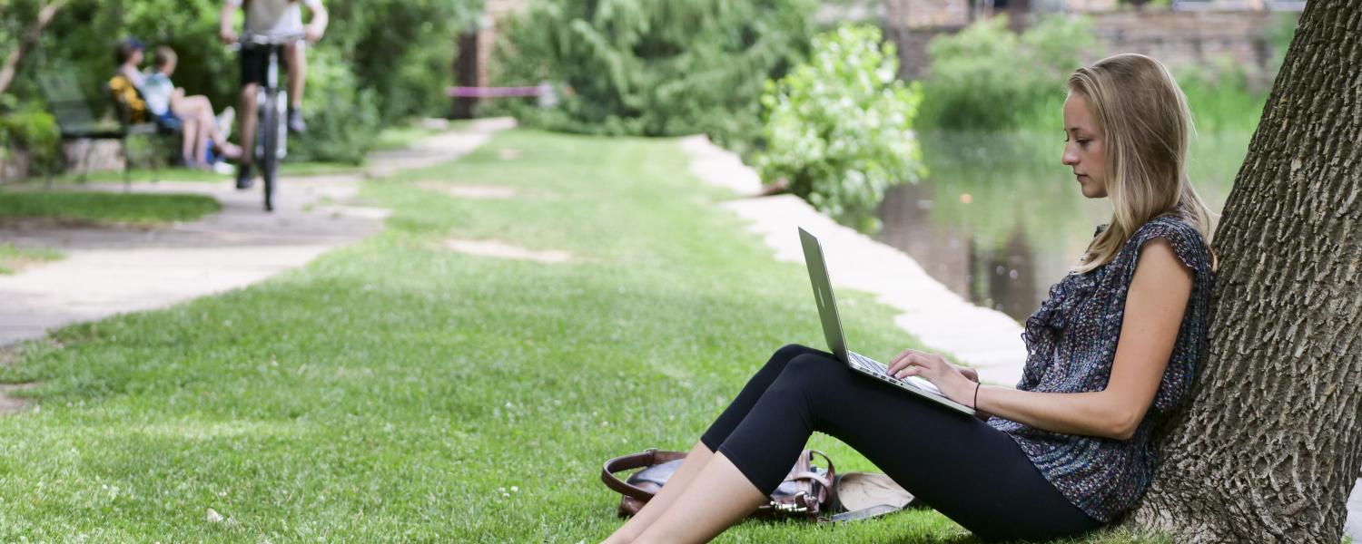 Grad student leans against a tree while working on laptop