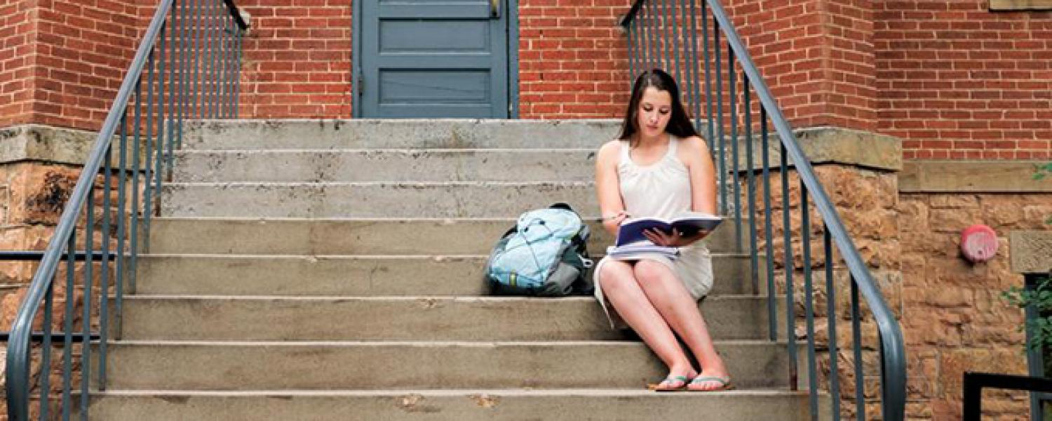 A woman sits on the steps of Old Main and reviews a notebook