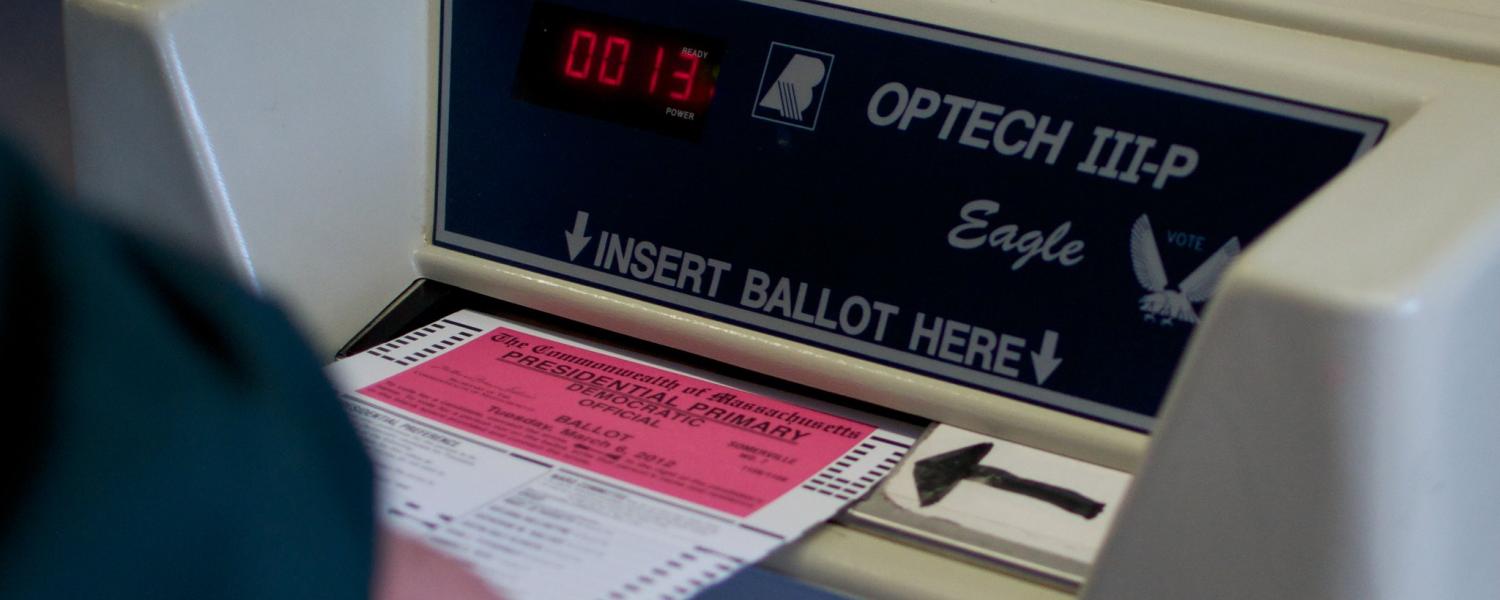 A person slides a ballot into an electronic voting machine.