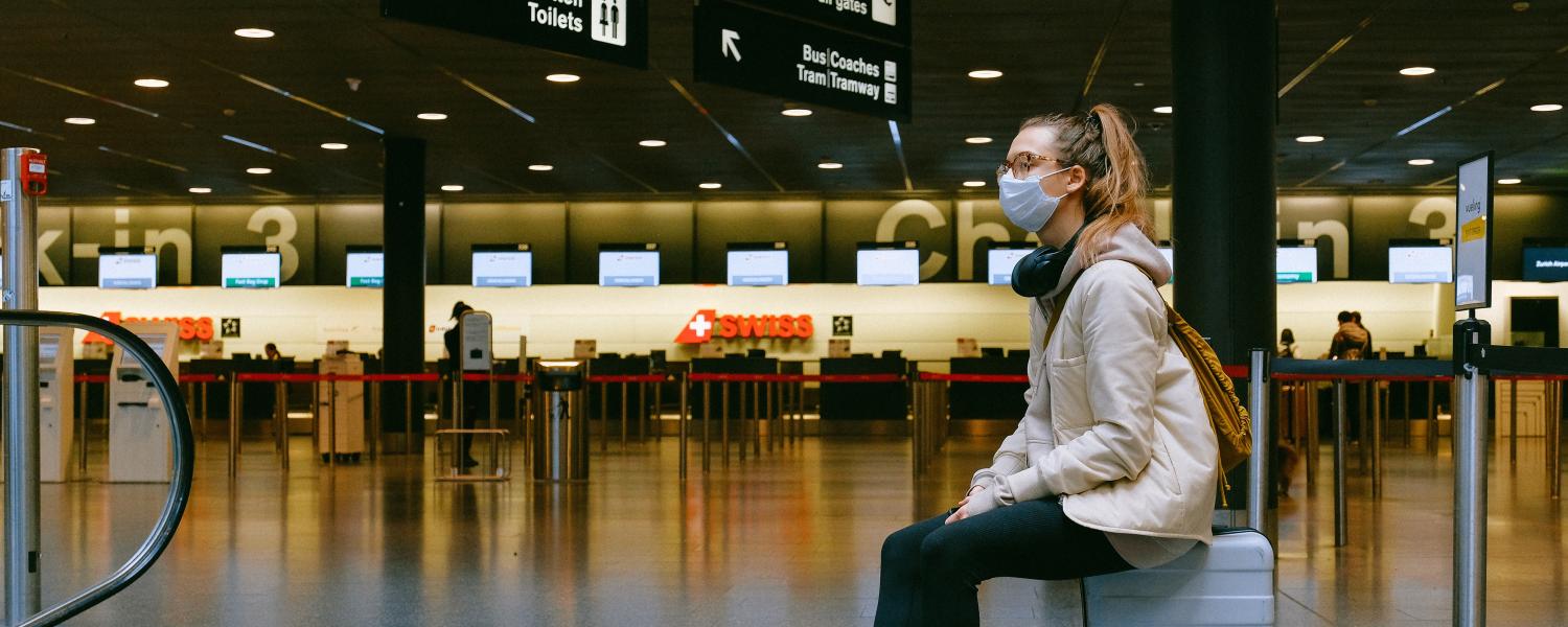 Woman sits in an airport while wearing a mask.