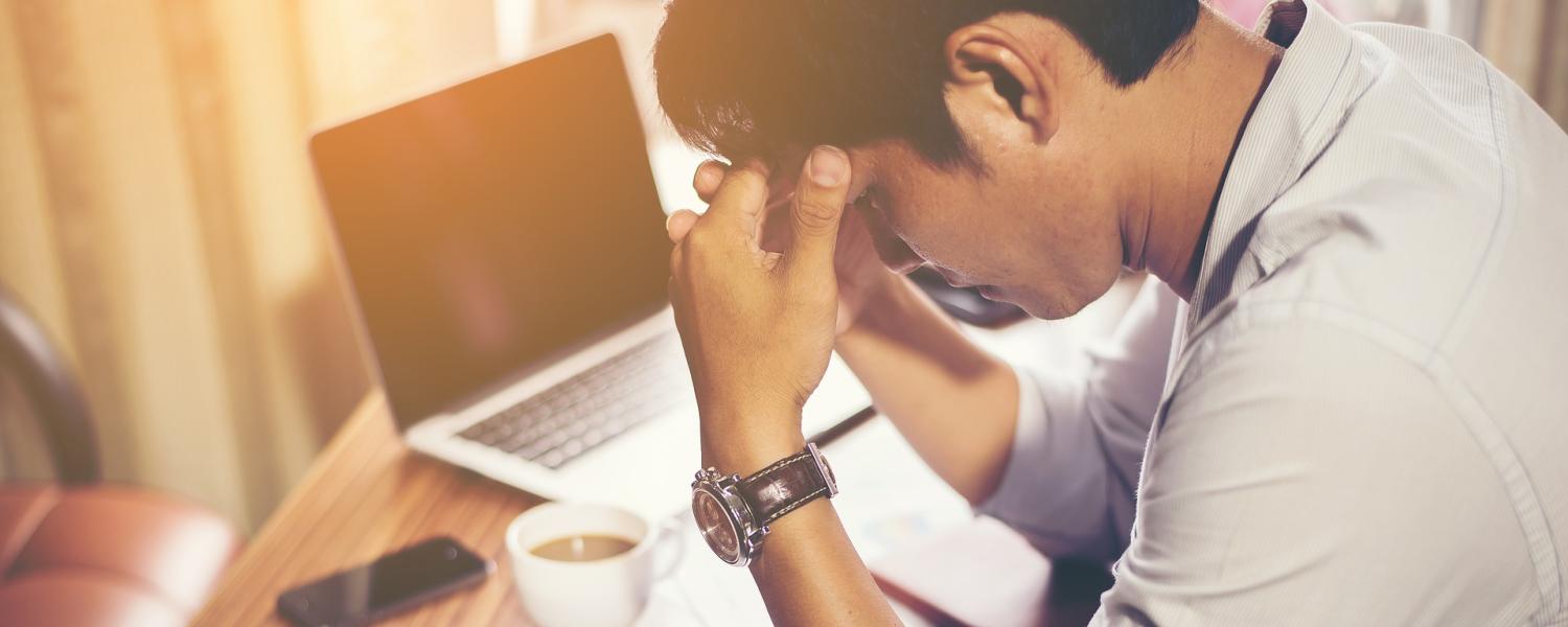 Man sitting at desk places head in hands