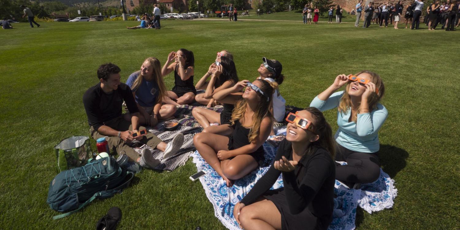 People sitting on grass wearing eclipse glasses and looking up