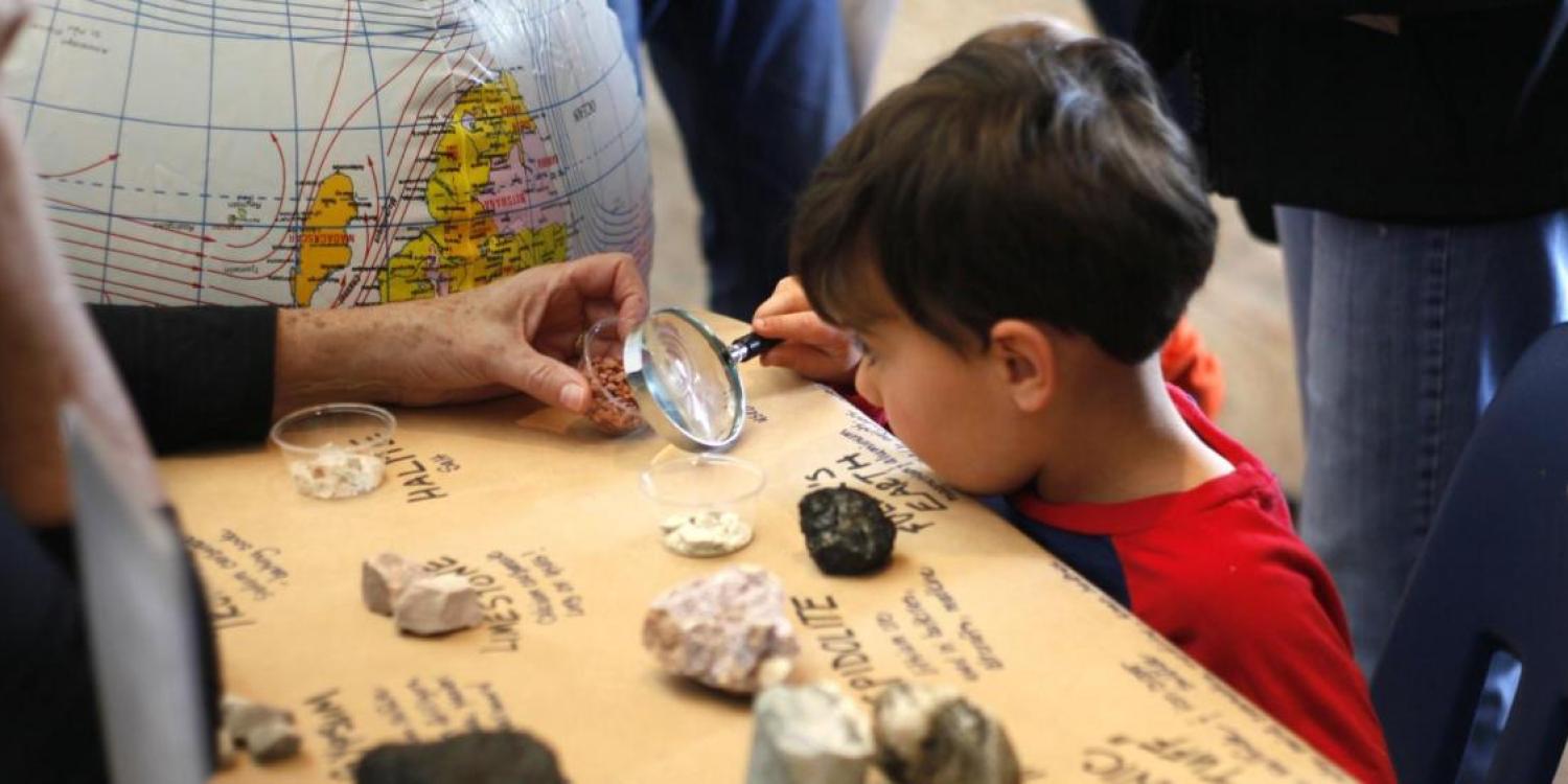 Child examines artifacts under magnifying glass