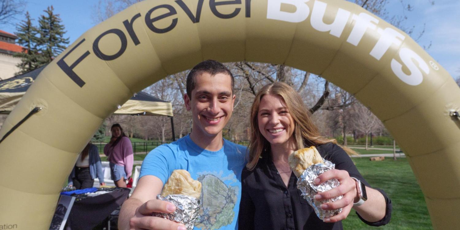 Two graduating students pose with free burritos in front of a Forever Buffs arch