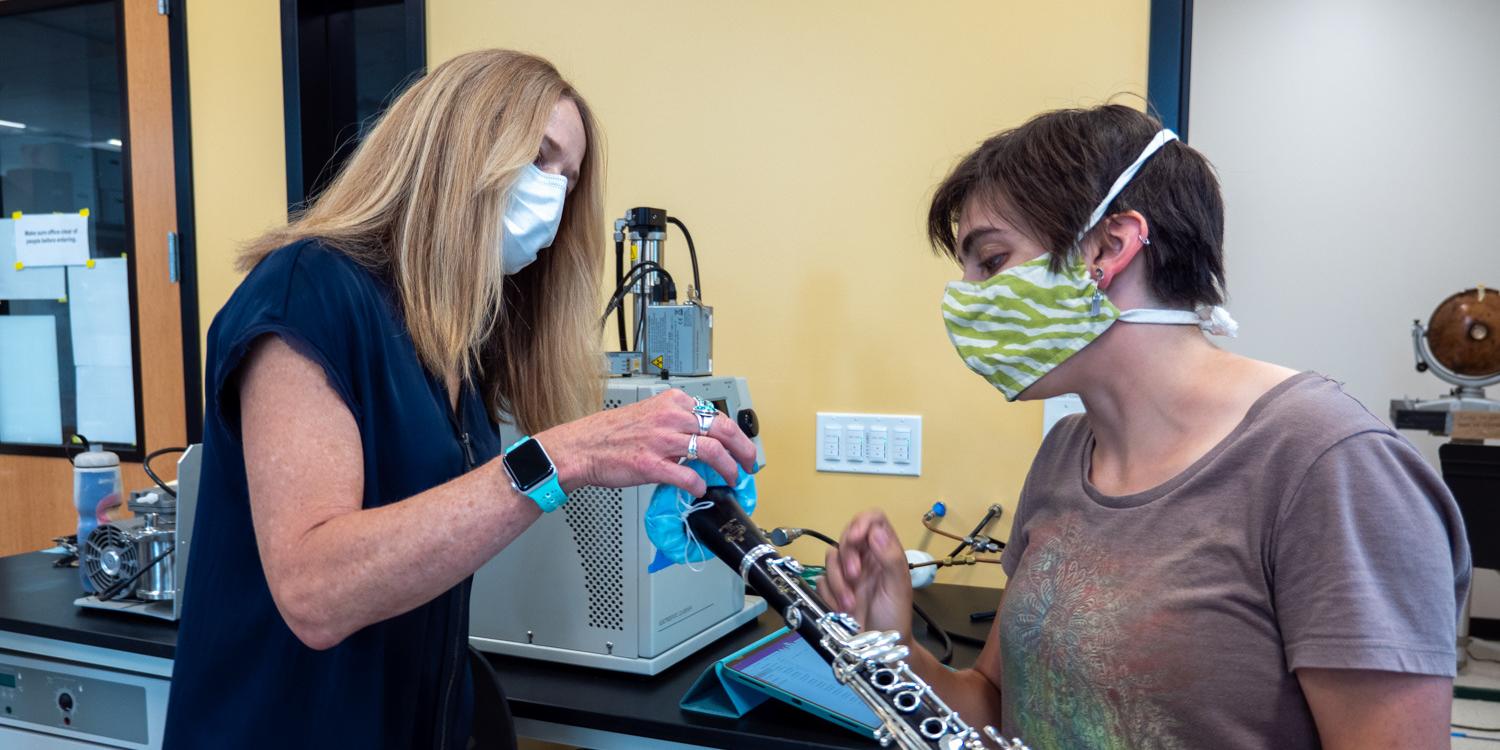 Graduate student Teyha Stockman, right, shows off her homemade bell cover made from medical mask material that helps decrease aerosol spread on her clarinet
