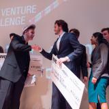 New Venture Challenge winner holds prize check and shakes hand with Professor Brad Bernthal