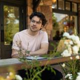 A person sits and looks out from a coffee shop patio.