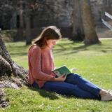 Student studying on lawn, leaned against a tree