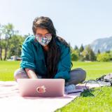 Student in mask working on laptop outside