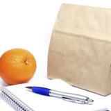 Brown Bag lunch next to a notepad, pen and orange