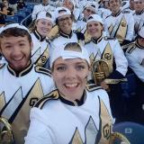 Marching band members in uniform and with their instruments pause for a selfie photo.