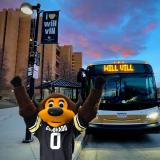 Chip the buffalo mascot with hands raised in front of a Buff Bus