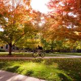 Person riding a bike on campus surrounded by fall foliage