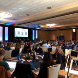 A large audience of people sit at tables during Destination Startup.