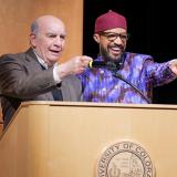 Chancellor Phil DiStefano and Professor Reiland Rabaka, smiling, point to the crowd from a podium