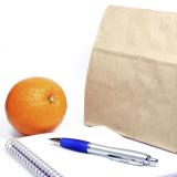 Brown-bag lunch, notebook, pen and an orange