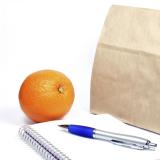 Brown bag lunch, notebook and pen, and an orange