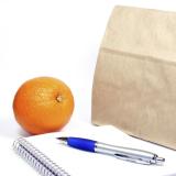Brown-bag lunch, notebook, pen and an orange