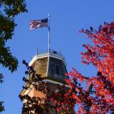 Flag flying atop Old Main building framed in red autumn leaves