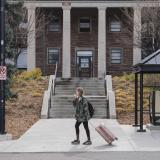 student with rolling suitcase departing campus for break