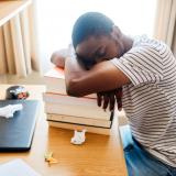 student sleeping on stack of books at desk