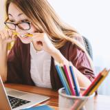 stressed out student bites pencil while looking at laptop computer