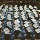 Graduates in caps and gowns sit facing stage at commencement ceremony