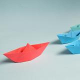 red paper boat leading other paper boats