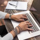 A persons hands and arms are poised to work at a laptop.