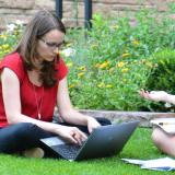 Two women sitting on lawn and working on laptop