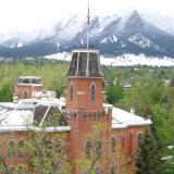 The Old Main building surrounded by the green foliage of spring trees, with snow-dusted foothills in the background.