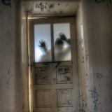 Sillhouette of hands pressed against a window in an old building