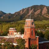 A bright sun reflects on the roof of Old Main and its surroundings, including the Flatirons in the background.
