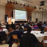 attendees sit at tables watching a past 3MT competition 