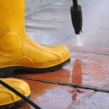 Person wearing yellow rubber boots and power washing the ground