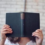 Person holds book in front of face. (Stock image.)
