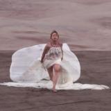 A woman in a white ball gown dances across a sandy expanse