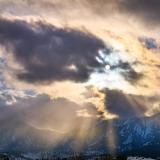 Sun peaks through clouds over snow-covered Flatirons