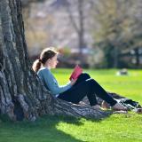 Student reading leaned against a tree on campus