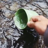 Woman dips drinking cup into fresh water source