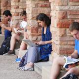 Students sit on a ledge and appear to be studying. 