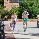 Student riding a bike on campus, while a friend walks alongside him