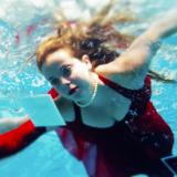Woman in red dress swimming through water with floating photographs