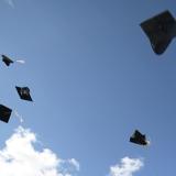 A number of graduation caps are suspended in air with a blue-sky backdrop.